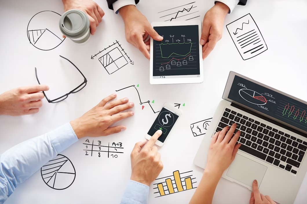 Business meeting with hands on table, laptop, and tablet.