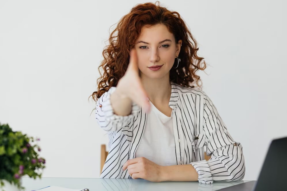 A woman working on her laptop extends her hand in a greeting gesture